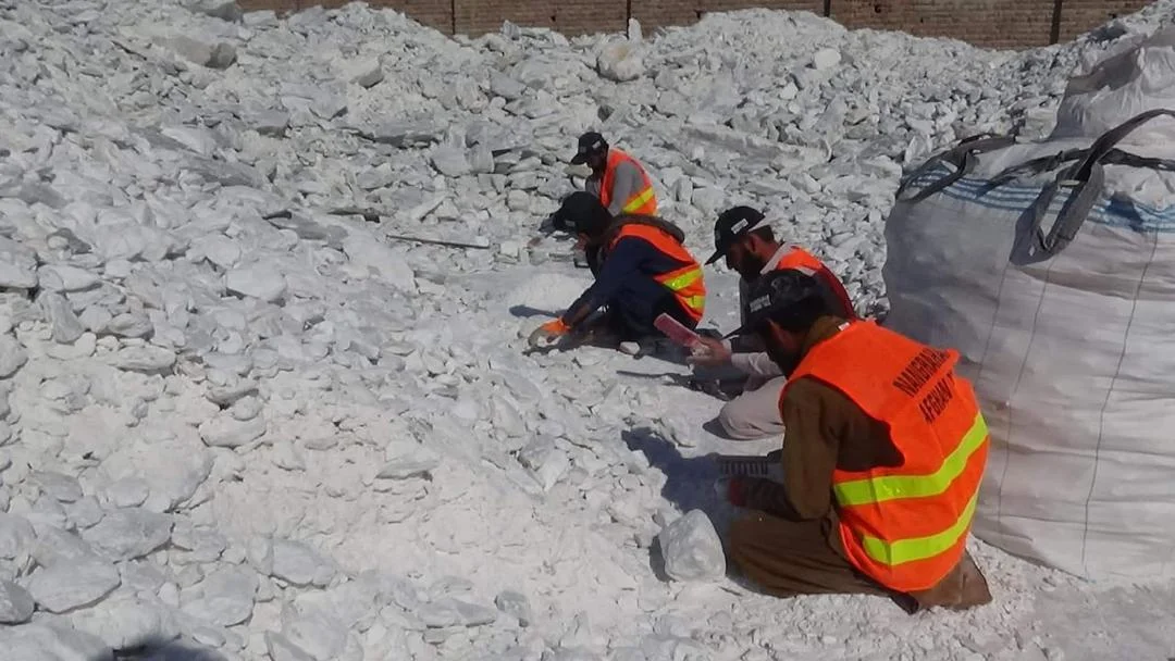 Workers manually selecting talc lumps beside packing bags